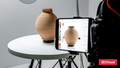 A 3D-rendered or photographed beige ribbed vase displayed on a white round table, with a smartphone showing the same vase and a camera on a tripod in the foreground. A red 3DCloud logo appears in the bottom-right corner.